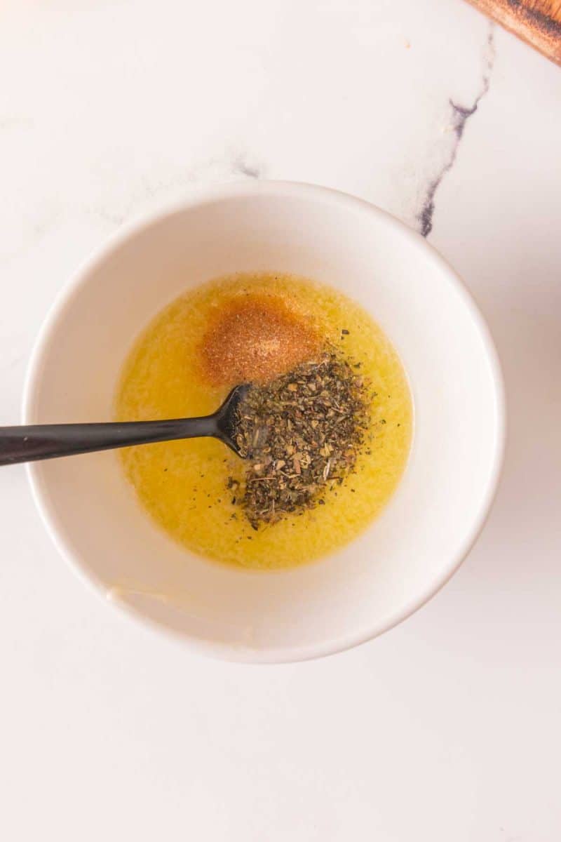 Small glass bowl with melted butter, Dijon mustard, and garlic powder being combined together. Hostess At Heart