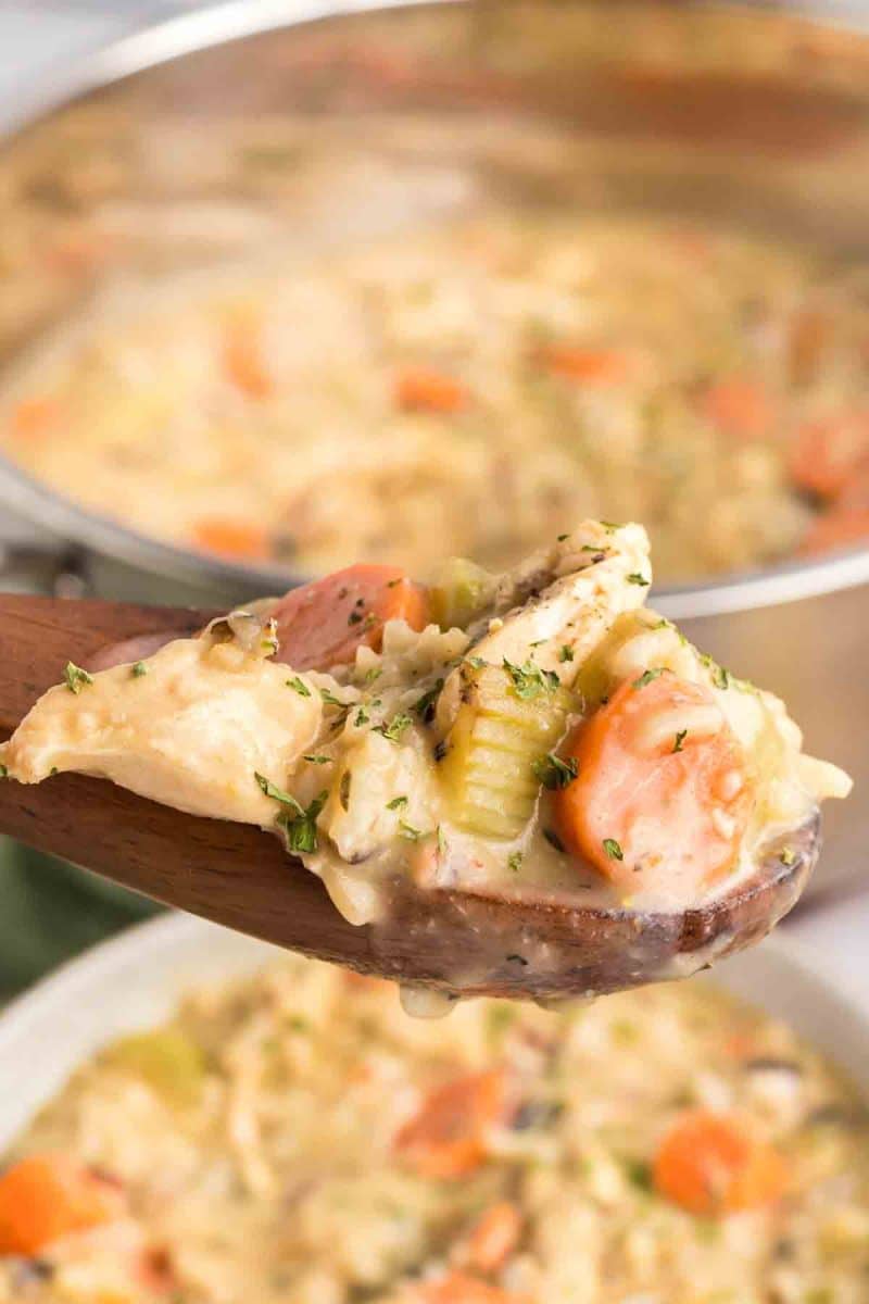 Sideview of a wooden spoon lifting a serving of thick and creamy chicken with wild rice and vegetable soup from the pot. Hostess At Heart