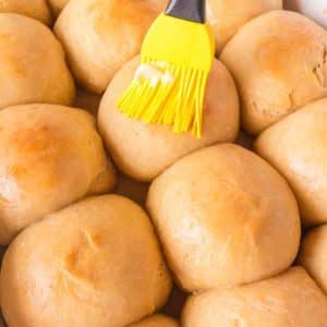 Close up of a basting brush applying butter to a pan of fluffy hawaiian rolls. Hostess At Heart