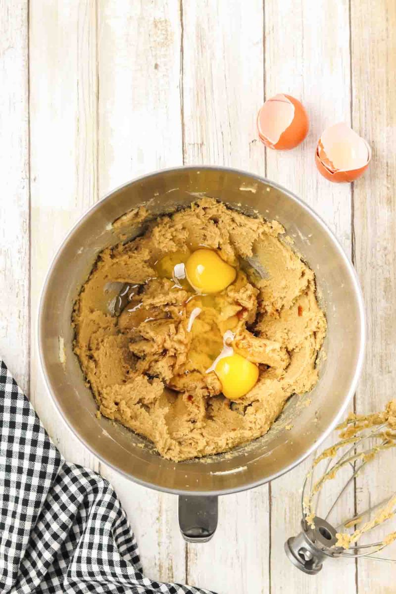Top down view of a medal mixing bowl filled with creamy cookie dough topped with two eggs ready to mix in. Hostess At Heart