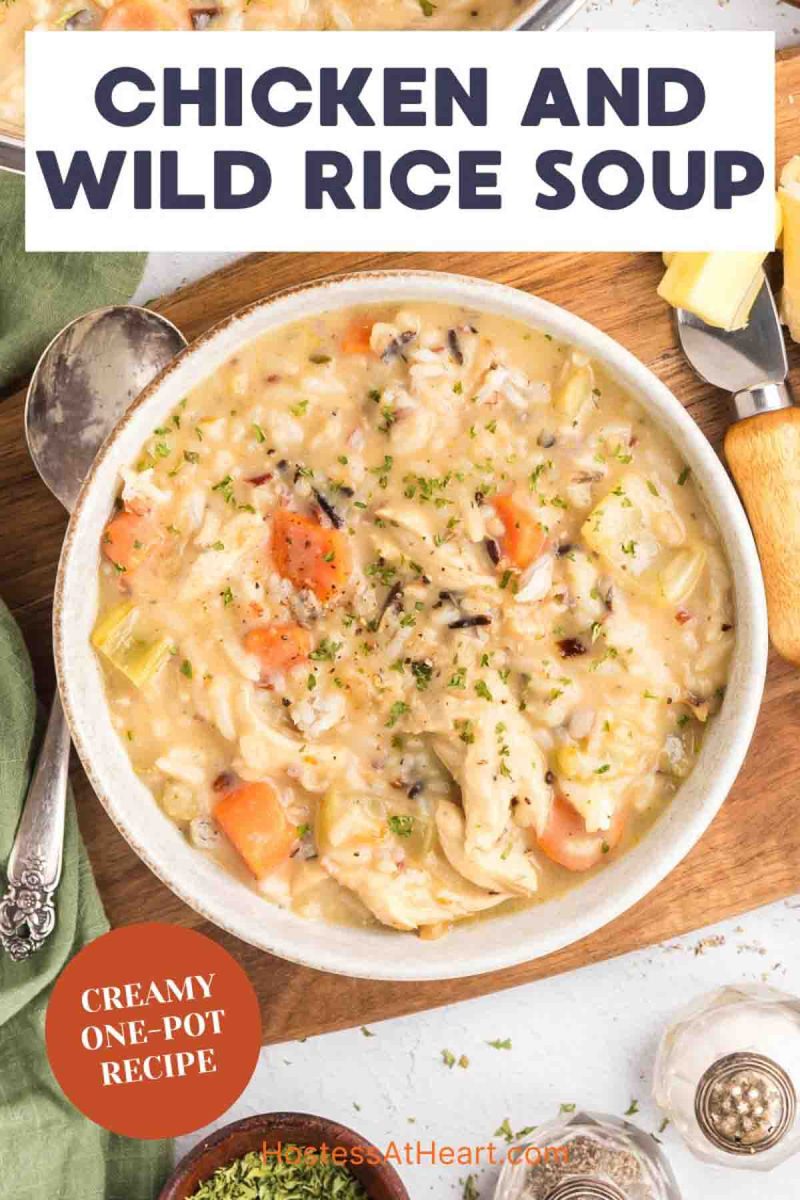 An image for photo of a bowl of creamy chicken and wild rice soup showing chunks of chicken, wild rice, and colorful vegetables in thick broth and garnished with herbs. Hostess At Heart