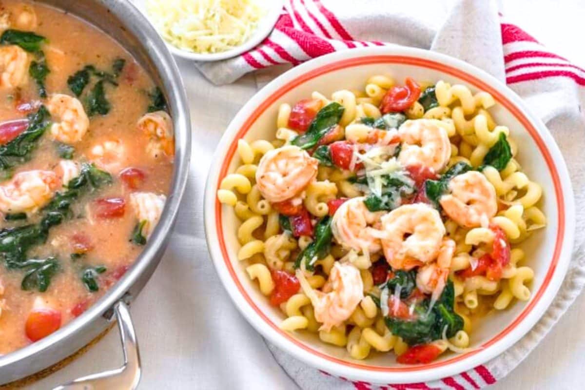 A bowl filled with our Creamy Shrimp Pasta recipe next to the skillet filled with the cooked  dish.