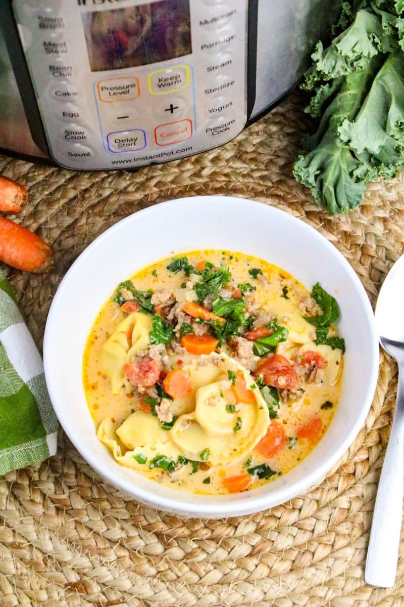 Top down view of a white bowl filled with creamy tortellini and Italian sausage soup. It's loaded with fresh chopped cale, spices, and chopped carrots - Hostess At Heart