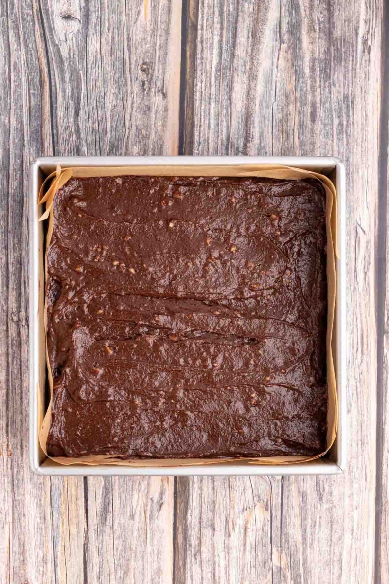 Gluten Free Brownie batter in a parchment paper-lined 8-inch baking pan. Hostess At Heart