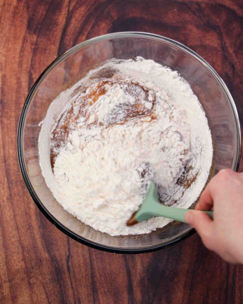 Flour being mixed into a mixing bowl filled with the wet chocolate pecan brownie batter ingredients. Hostess At Heart