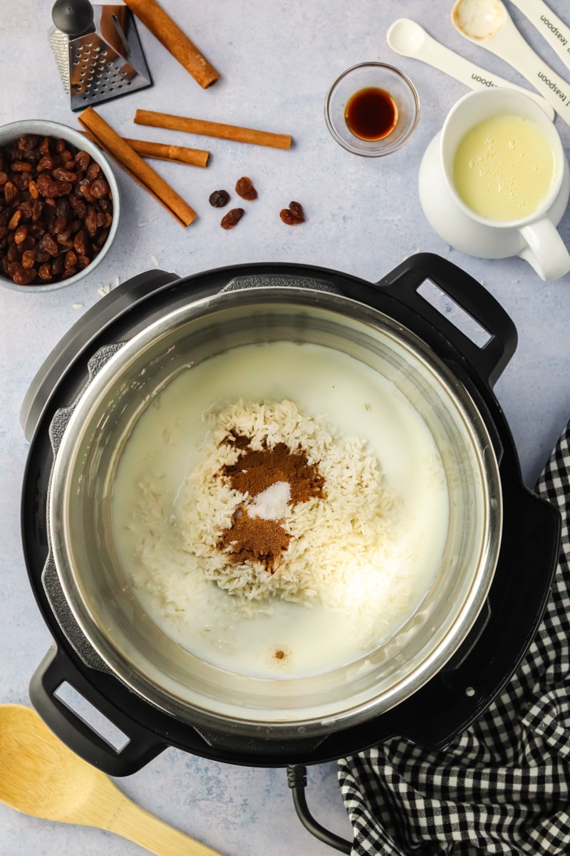 Top down view of an instant pot filled with water, milk, rice, cinnamon, and nutmeg in order to make rice pudding instant pot recipe - Hostess at Heart