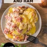 An image for Pinterest of a single serving of scalloped potatoes with ham on plate showing tender potato layers and diced ham in creamy sauce - Hostess At Heart