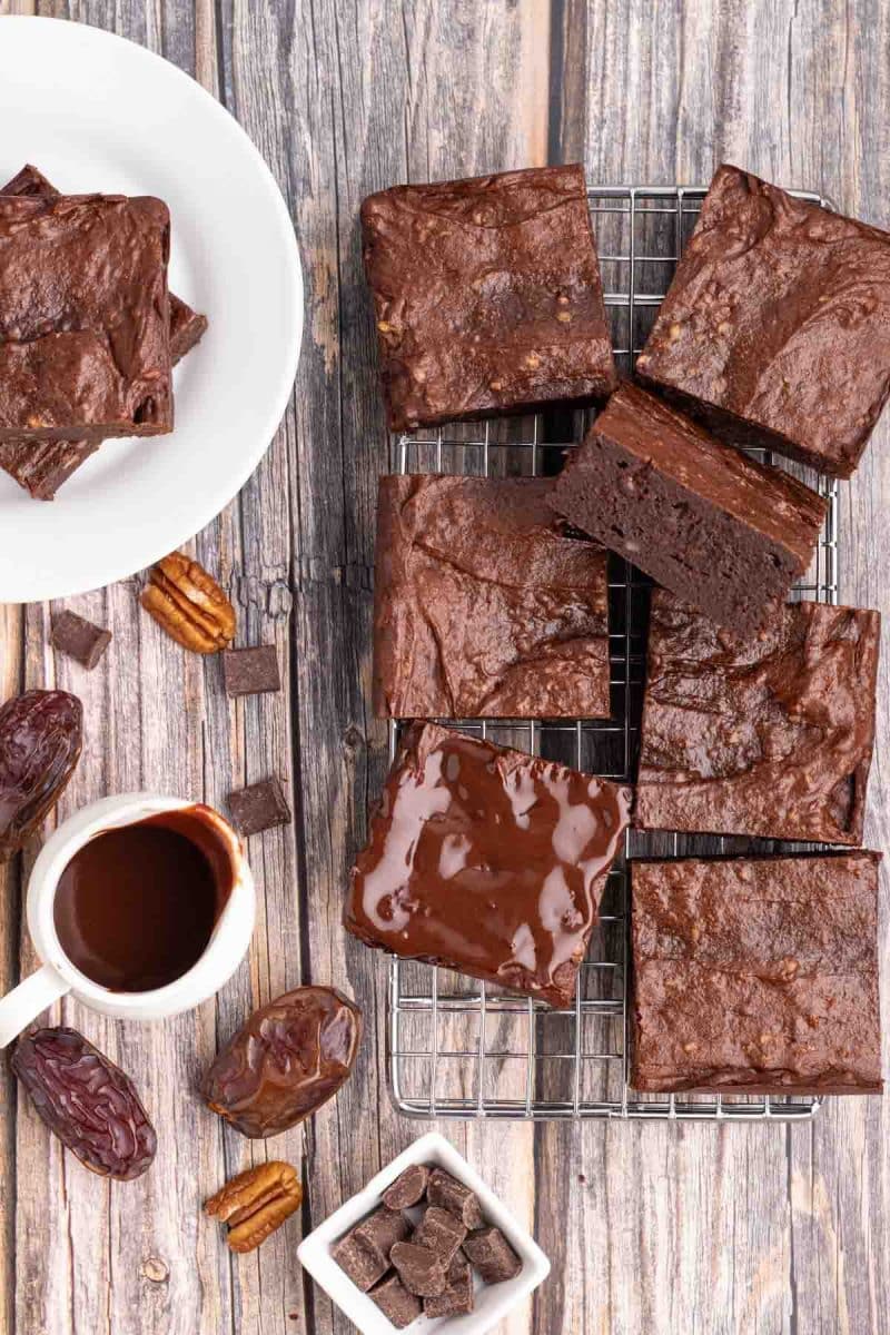 Top down view of cut squares of gluten free brownies sitting on a cooling rack. One brownie is topped with glossy dairy free chocolate granache - Hostess At Heart