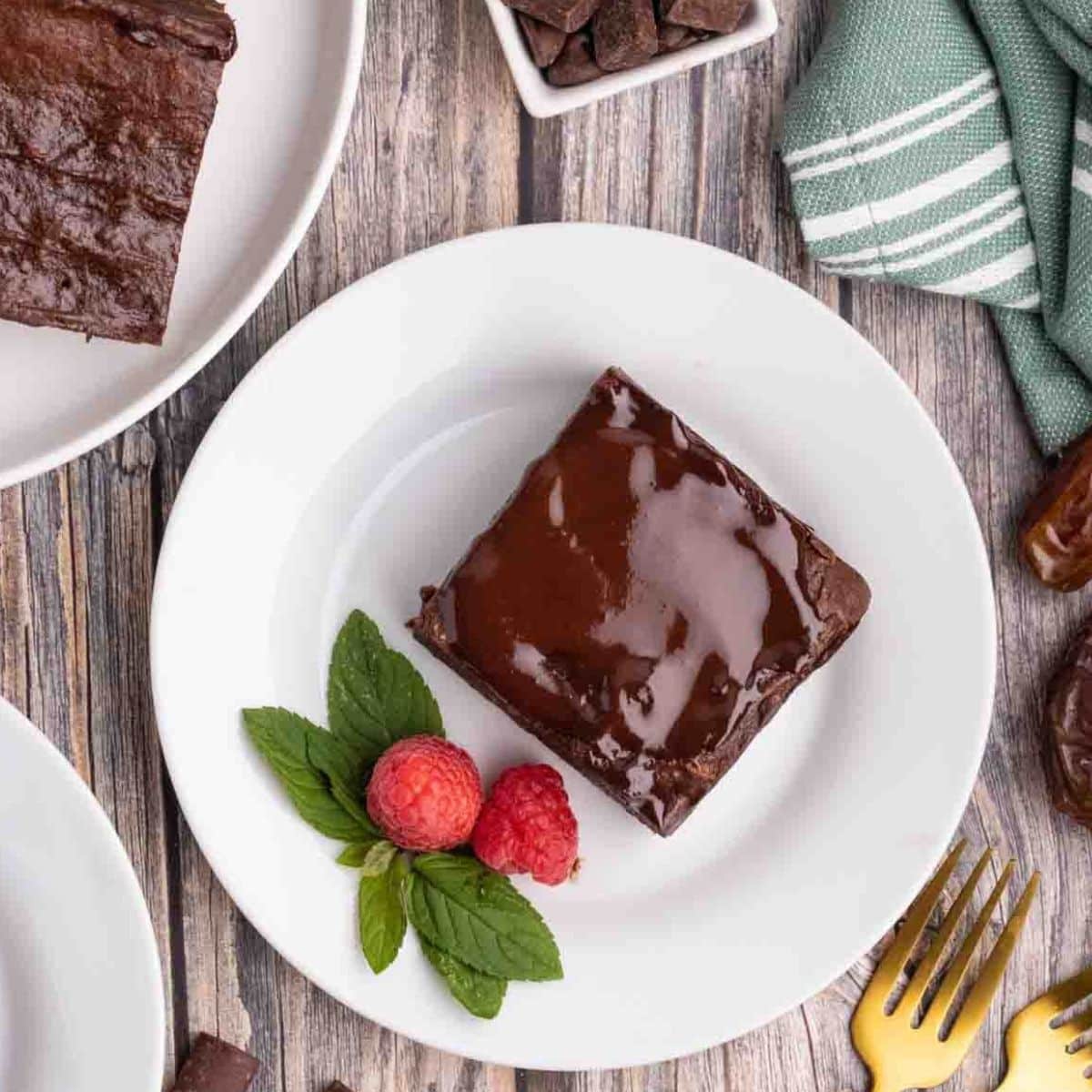 Top down view of a piece of gluten free chocolate brownie topped with fudgy ganache on a white plate garnished with raspberries and mint - Hostess At Heart