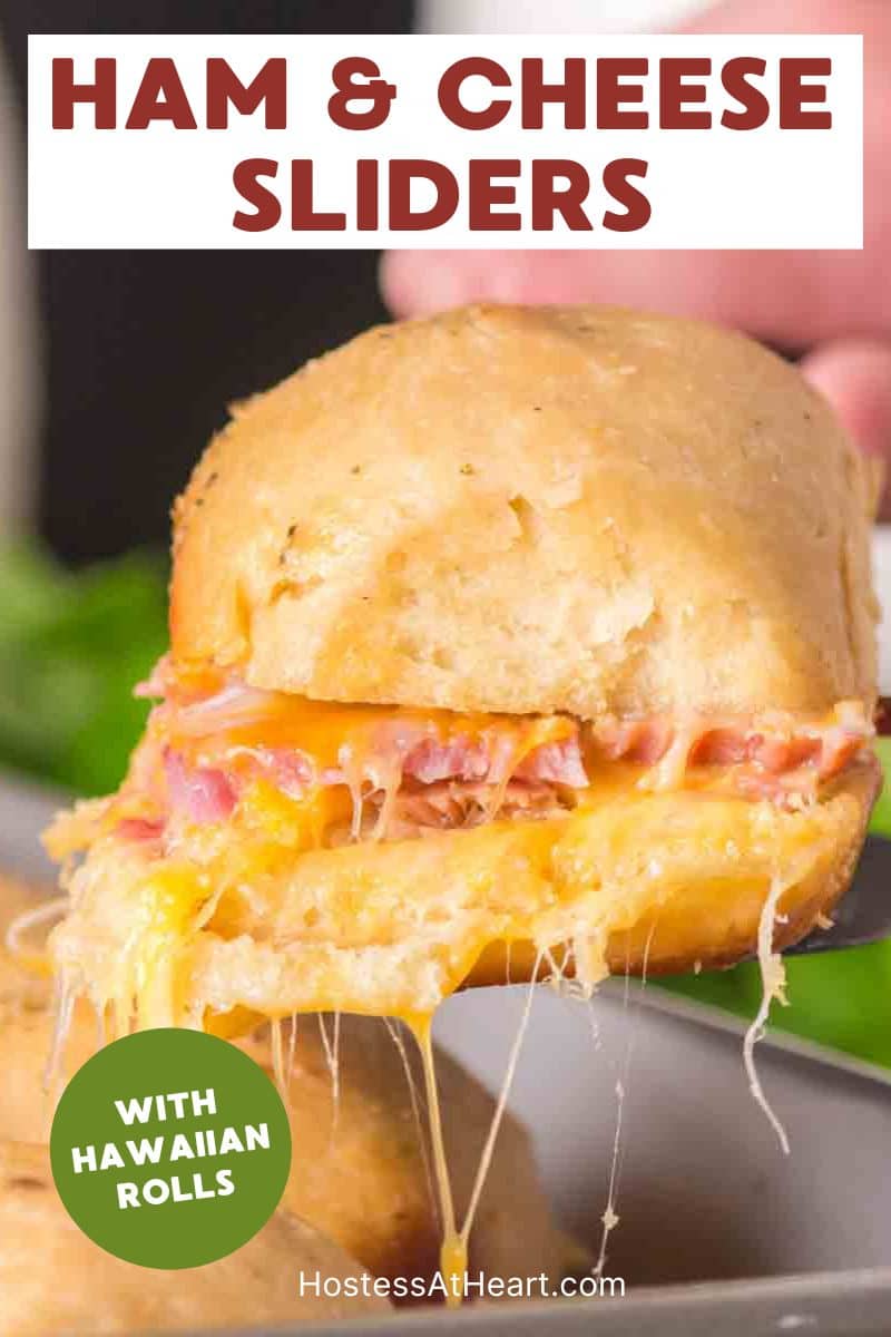 An image for Pinterest of a hand holding a Hawaiian Roll Ham and Cheese slider showing a layer of ham and stretching melted cheese. Hostess At Heart