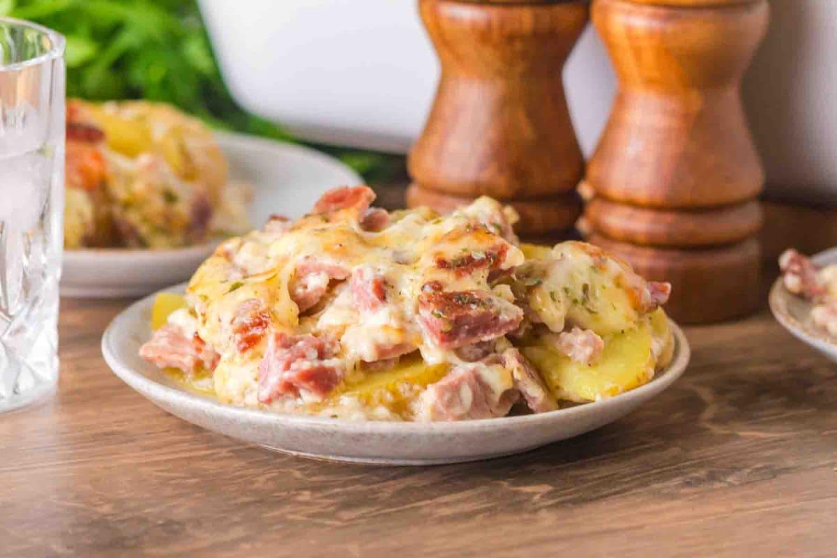 Side view of scalloped potatoes with ham showing distinct layers of potatoes, ham, and bubbling golden cheese - Hostess At Heart