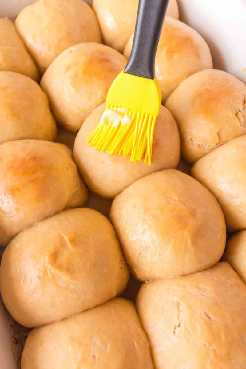 A basting brush applying soft butter to the tops of warm golden brown baked Hawaiian Rolls - Hostess At Heart