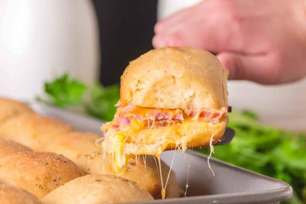 Hawaiian ham and cheese slider lifted from the pan to show stretchy melted cheese - Hostess At Heart