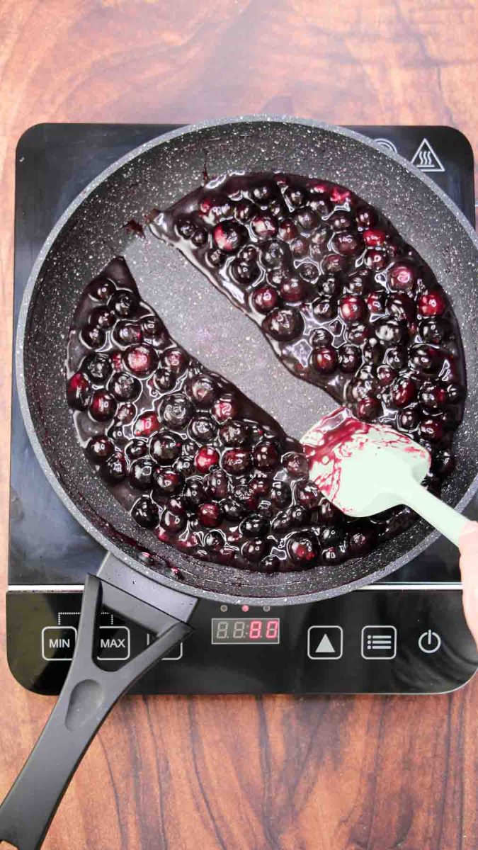 A rubber spatula pulled across a skilled of cooked blueberry filling showing the proper thickness - Hostess At Heart