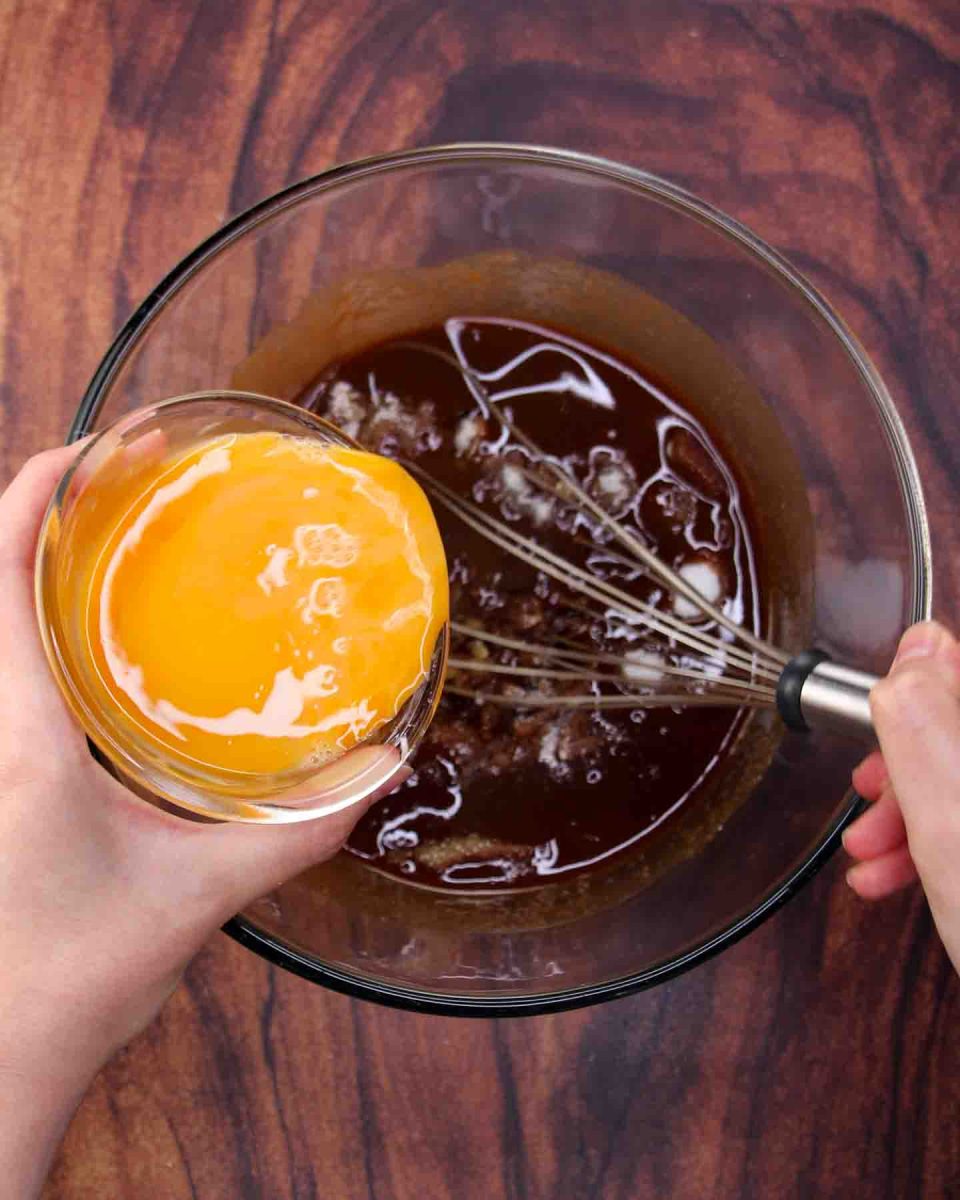 Beaten eggs added to a mixing bowl filled with a smooth mixture of melted butter and chocolate chips - Hostess At Heart