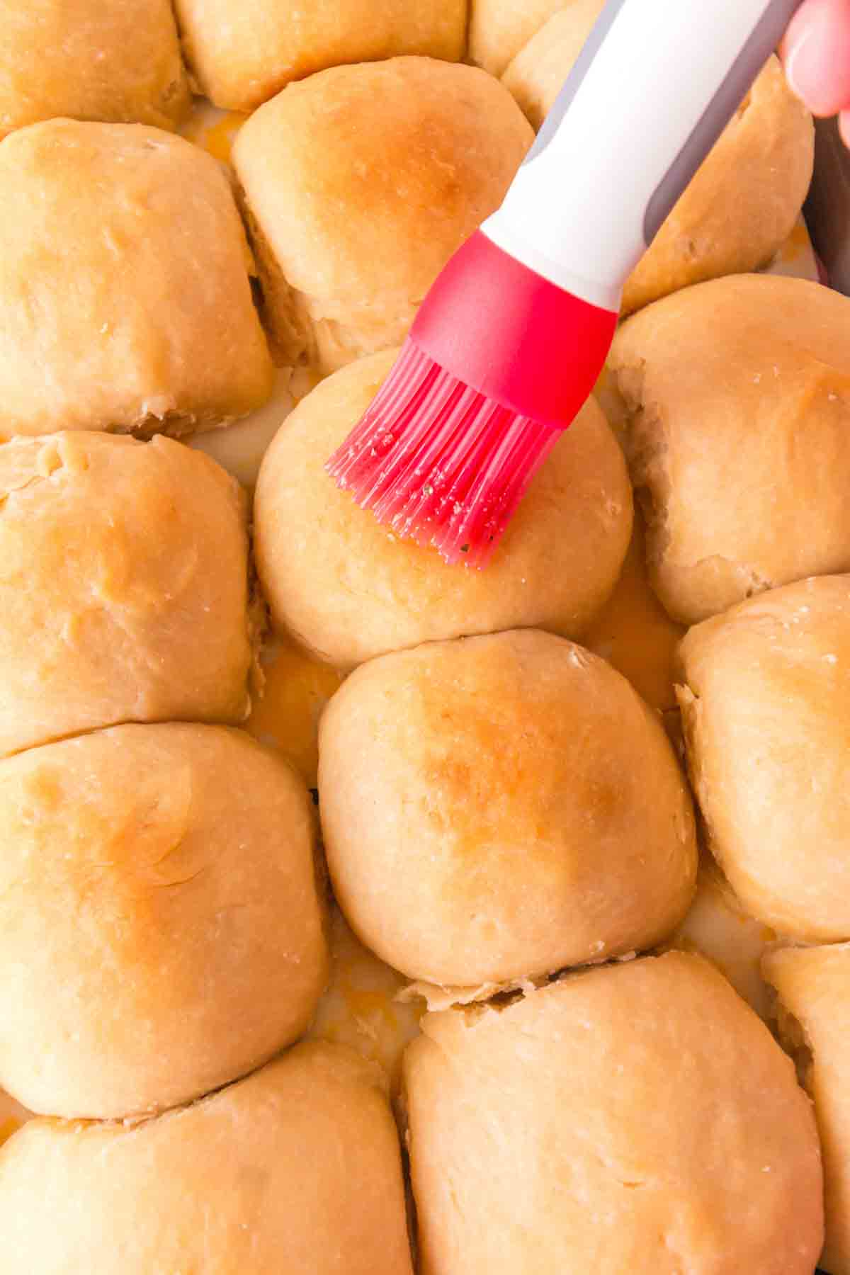 Brushing garlic herb butter mixture on top of assembled Hawaiian ham and cheese sliders. Hostess At Heart