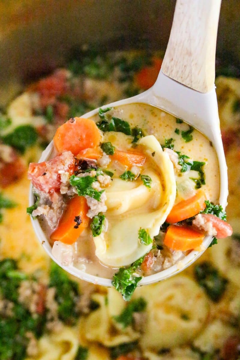 A ladle filled with a serving of Italian sausage tortellini soup hovering over an instant pot filled with the soup - Hostess At Heart