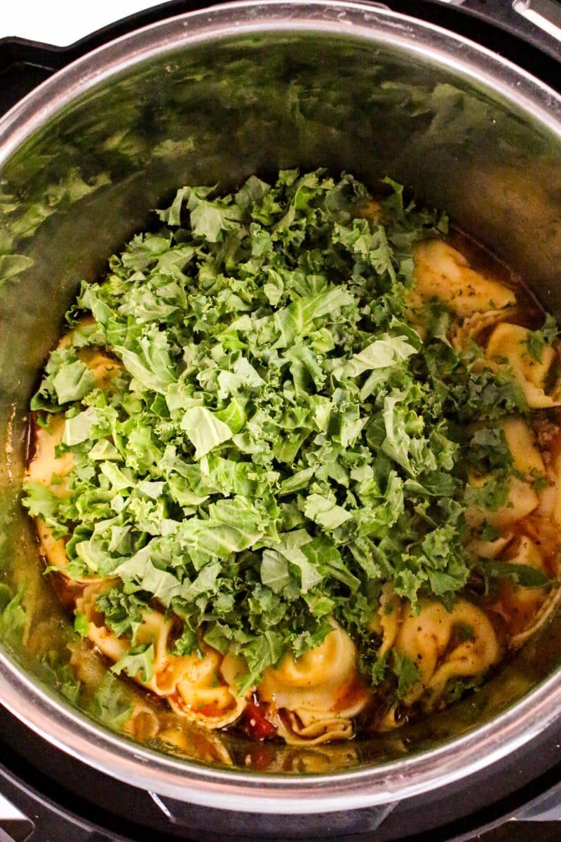 Chopped kale added to an instant pot filled with cheese tortellini sausage soup - Hostess At Heart
