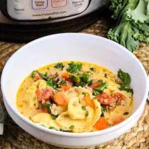 A bowl of Italian Sausage cheese tortellini soup in a creamy broth and wilted kale in white bowl. Hostess At Heart