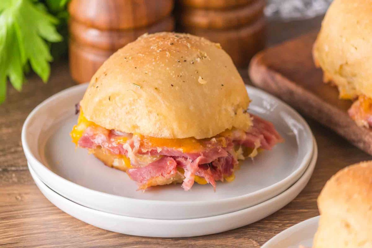 Side view of one Hawaiian ham and cheese slider on white plate showing layers of ham and melted cheese. Hostess At Heart