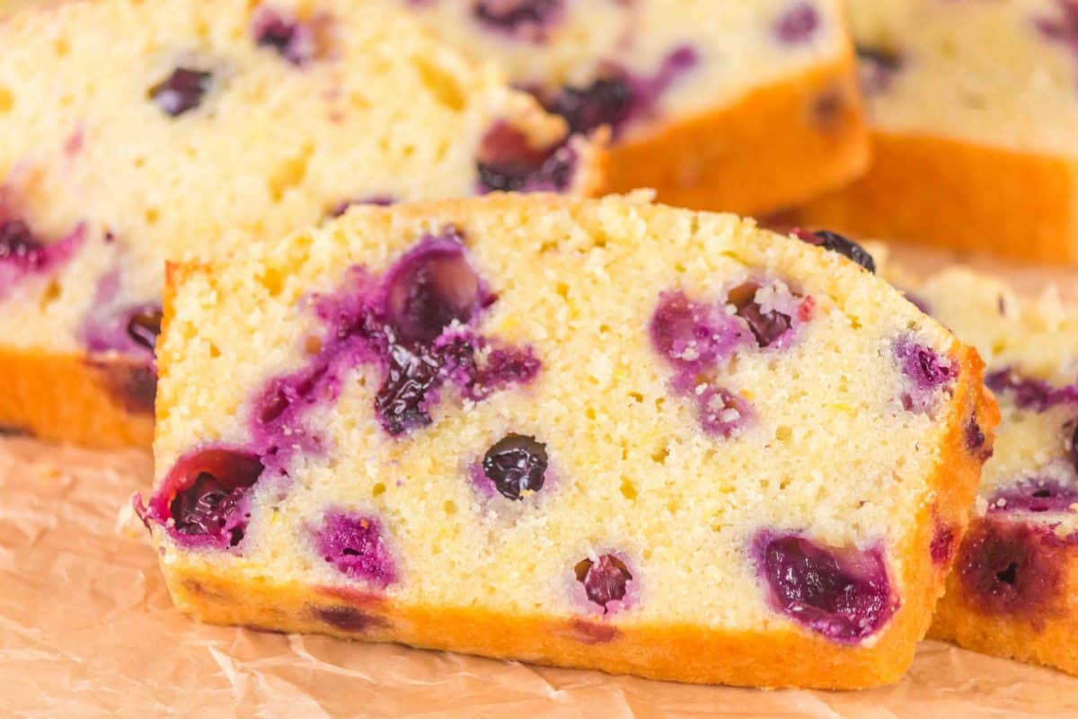 Slices of lemon blueberry sourdough bread showing tender crumb and blueberries sitting on a cutting board - Hostess At Heart