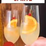 2 finished Limoncello Spritz cocktails in champagne glasses garnished with a orange wheel and, showing the pale yellow bubbly drink - Hostess At Heart