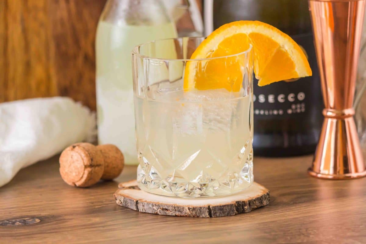 Finished Limoncello Spritz cocktail in a white wine glass garnished with a orange wheel and, showing the pale yellow bubbly drink - Hostess At Heart