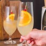 Finished Limoncello Spritz cocktail in a champagne glass garnished with a orange wheel and, showing the pale yellow bubbly drink - Hostess At Heart