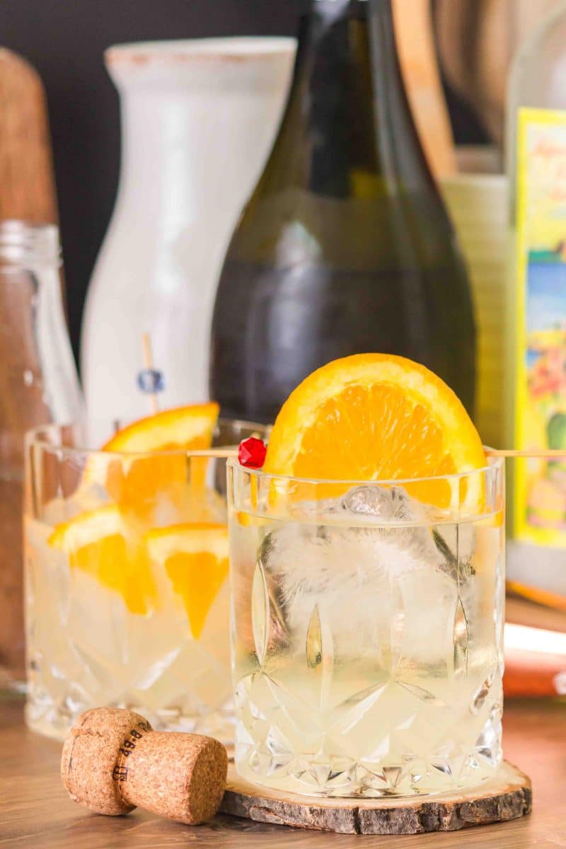 Finished Italian Spritz cocktail in a rocks glass garnished with a orange wheel, showing the pale yellow bubbly drink. Hostess At Heart