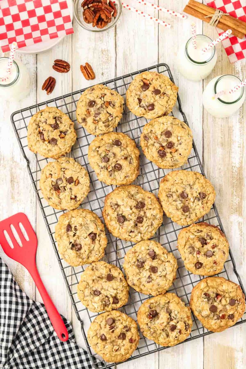 Top down view of a cooking rack filled with golden brown cowboy cookies loaded with chocolate chips, oats, and pecans fresh from the oven. Hostess At Heart