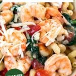 Image for Pinterest. Top down view of a bowl of Cavatappi pasta loaded with jumbo shrimp, tomatoes, and fresh spinach - Hostess At Heart