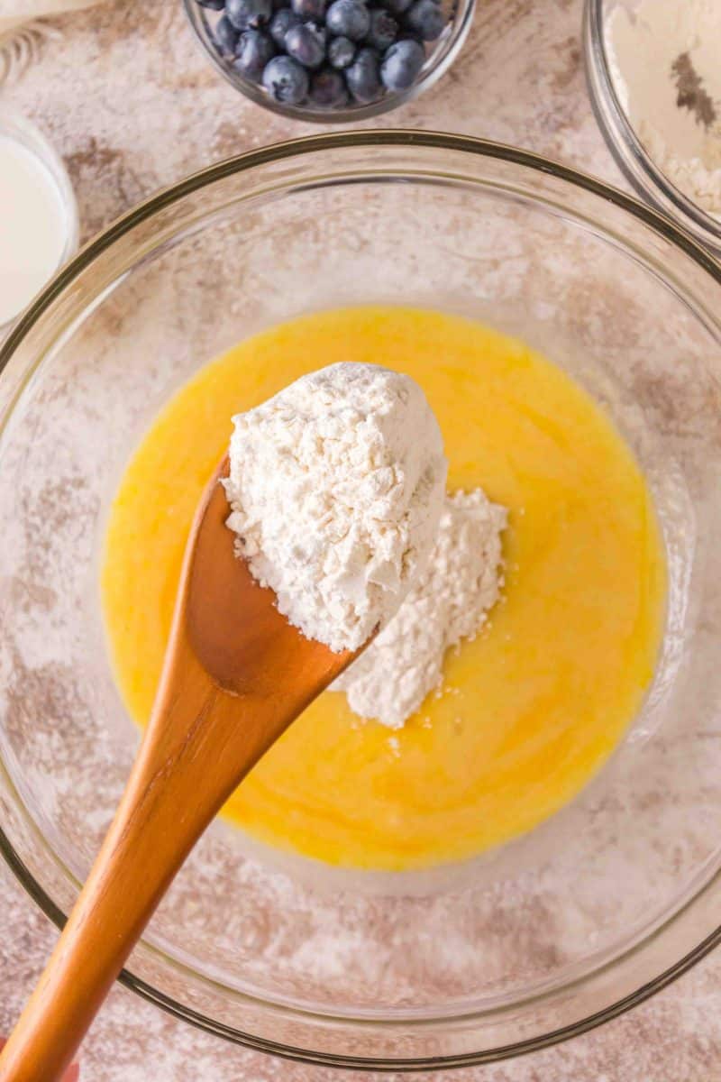 Dry ingredients spooned into a mixing bowl filled with blueberry bread wet ingredients - Hostess At Heart