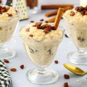 Sideview of three dessert dishes filled with Instant Pot Rice Pudding filled with spices and raisins - Hostess At Heart