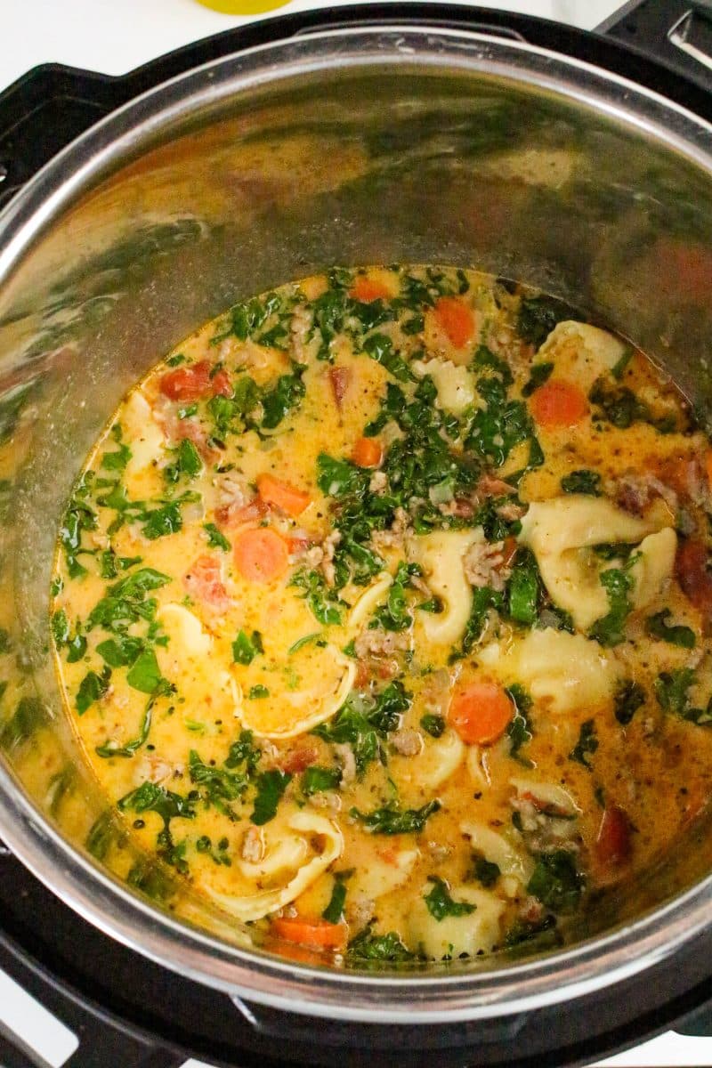 Stirring cream and fresh kale into Italian sausage tortellini soup after pressure cooking - Hostess At Heart