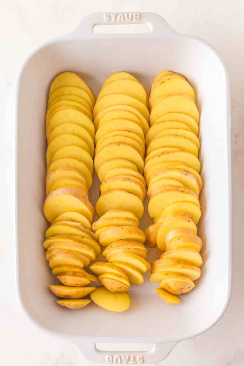 Sliced unpeeled golden potatoes in a white baking dish - Hostess At Heart