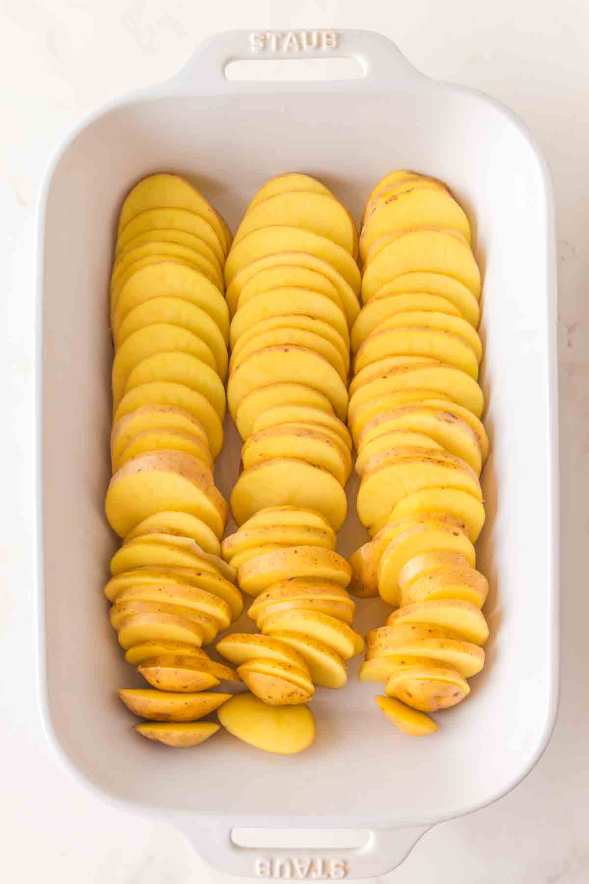 Sliced unpeeled golden potatoes in a white baking dish - Hostess At Heart