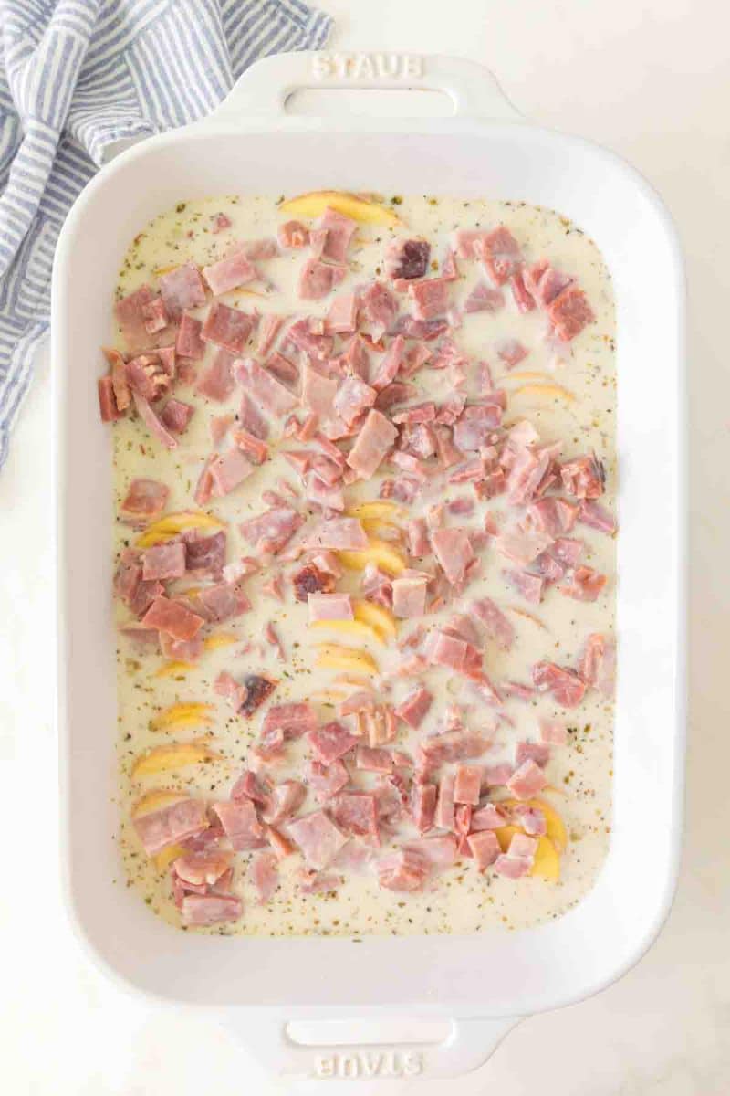 Creamy sauce with ham over layer of sliced potatoes in 9x13 baking dish before baking - Hostess At Heart