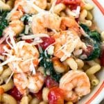 Top down view of a bowl of Cavatappi pasta loaded with jumbo shrimp, tomatoes, and fresh spinach garnished with cheese - Hostess At Heart
