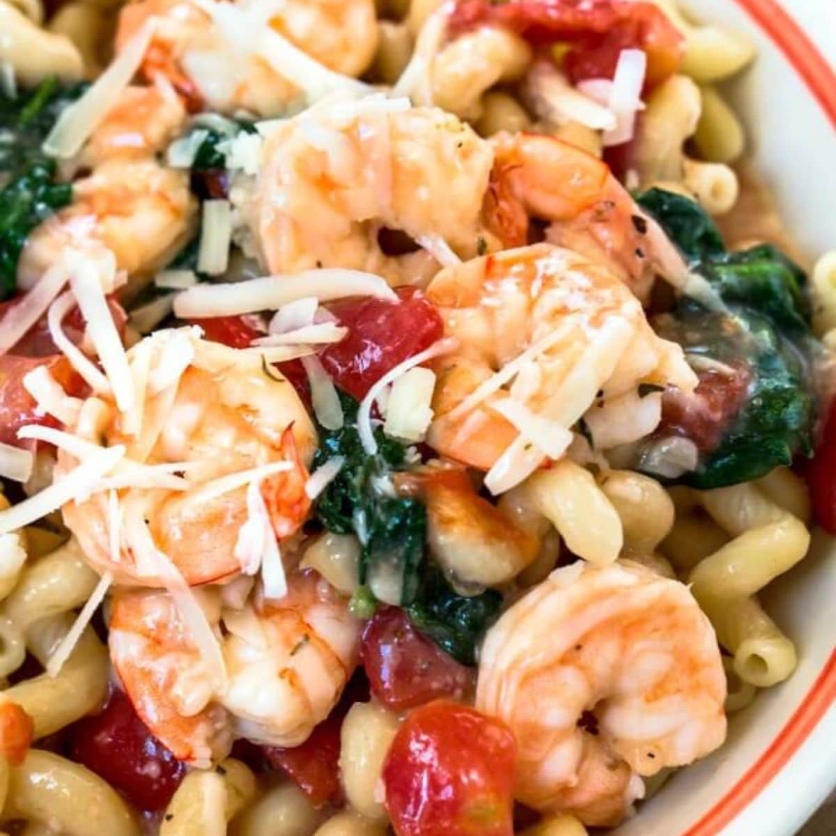 Top down view of a bowl of Cavatappi pasta loaded with jumbo shrimp, tomatoes, and fresh spinach garnished with cheese - Hostess At Heart