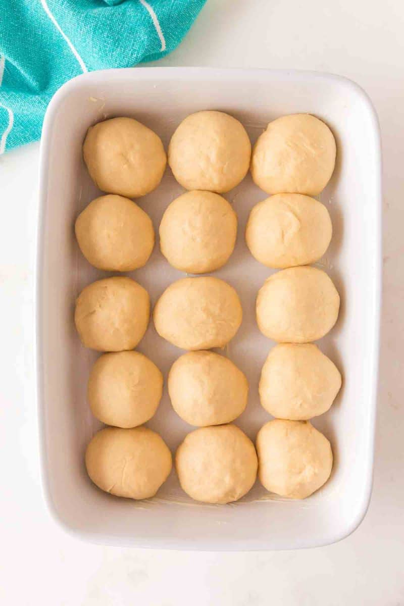 Fifteen unbaked hawaiian roll dough balls arranged in greased 9x13 baking pan before second rise - Hostess At Heart