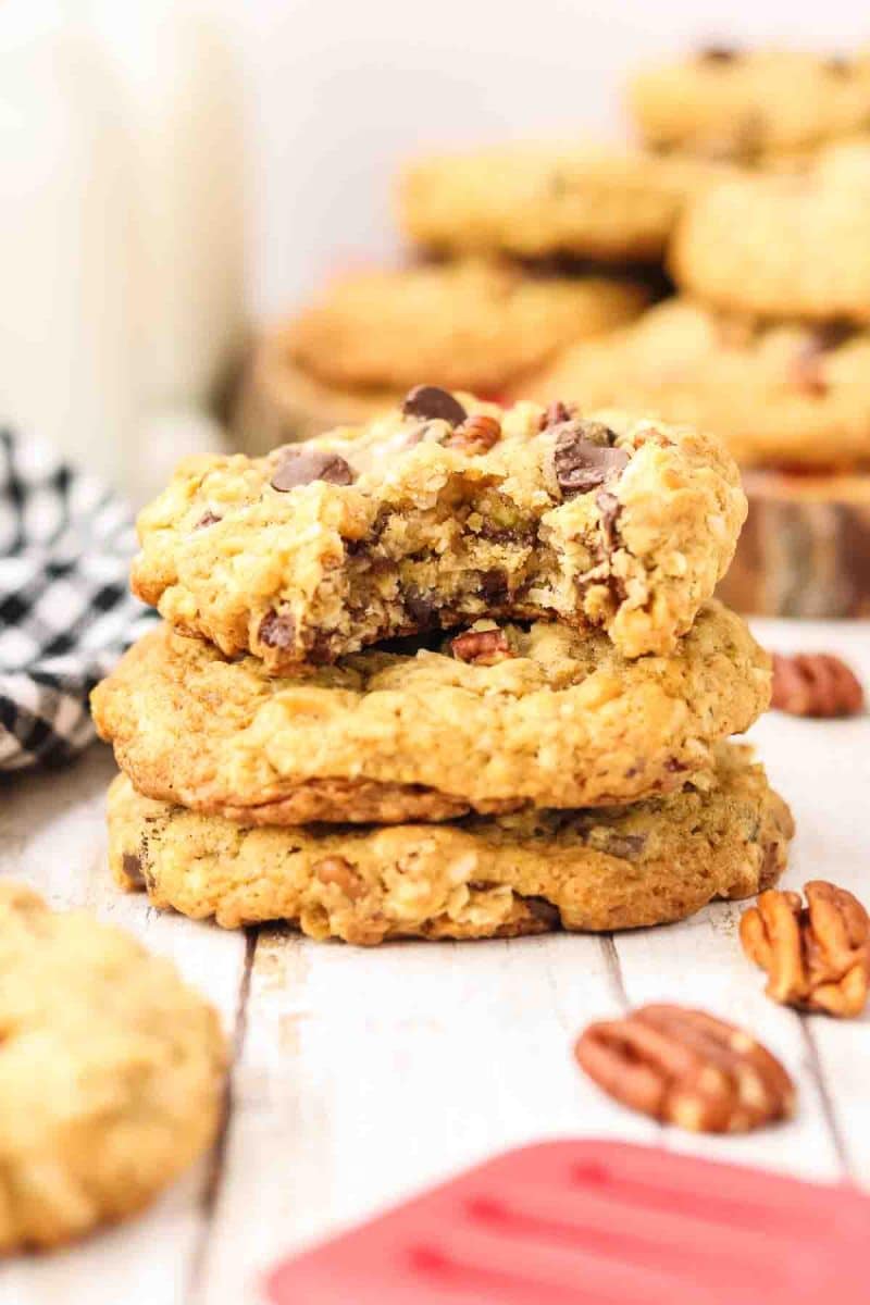 A stack of three golden-brown cowboy cookies with a bite taken out of the top one showing a tender interior dotted with chocolate chips, oats, and pecans.