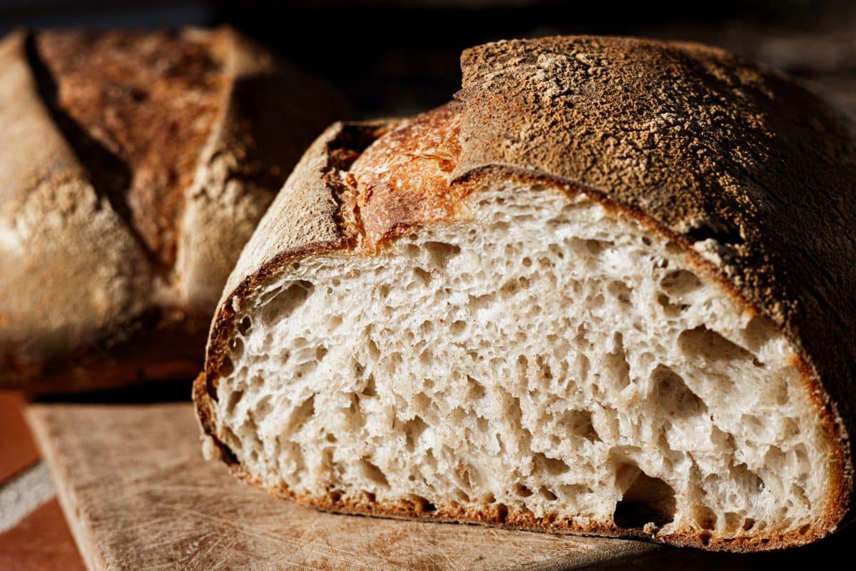 A loaf of sourdough bread cut in half showing an open soft crumb. Hostess At Heart