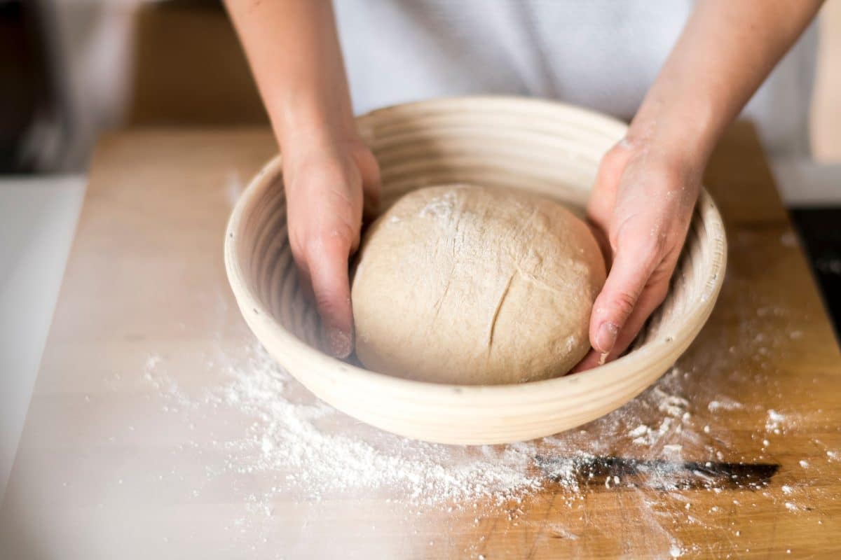 A ball of dough shaped and being placed in a banneton basket for fermentation. Hostess At Heart