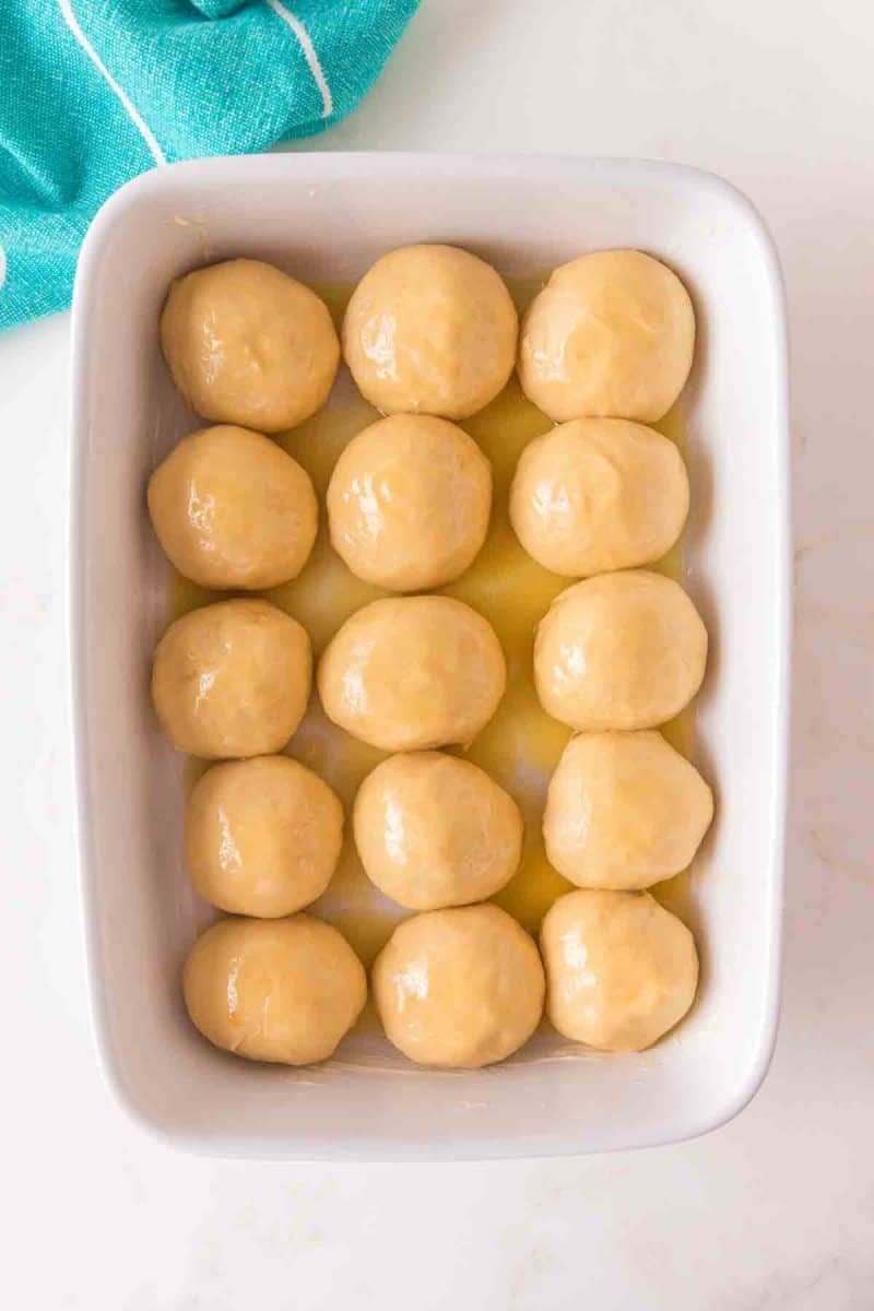 Pastry brush applying honey butter mixture to tops of risen hawaiian roll dough - Hostess At Heart