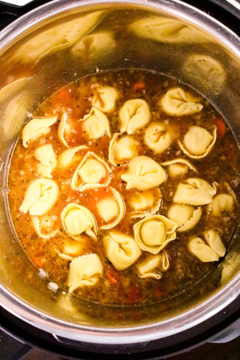 Cheese tortellini being added on top of soup ingredients in Instant Pot before pressure cooking - Hostess At Heart