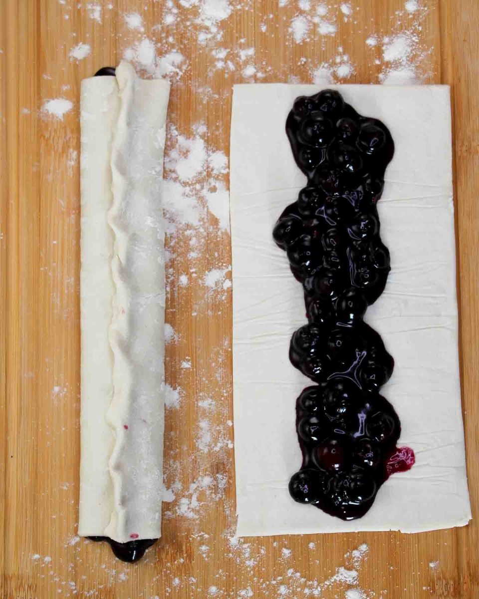 Top down view of puff pastry filled with blueberry filling. One is already rolled and crimped. The other one just has the filling poured over it - Hostess At Heart