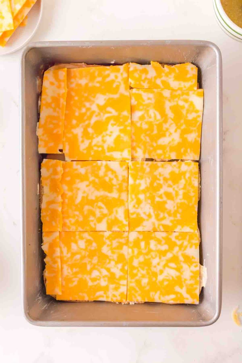 Placing Colby Jack cheese slices on buttered Hawaiian roll bottoms in a 9x13 baking dish. Hostess At Heart