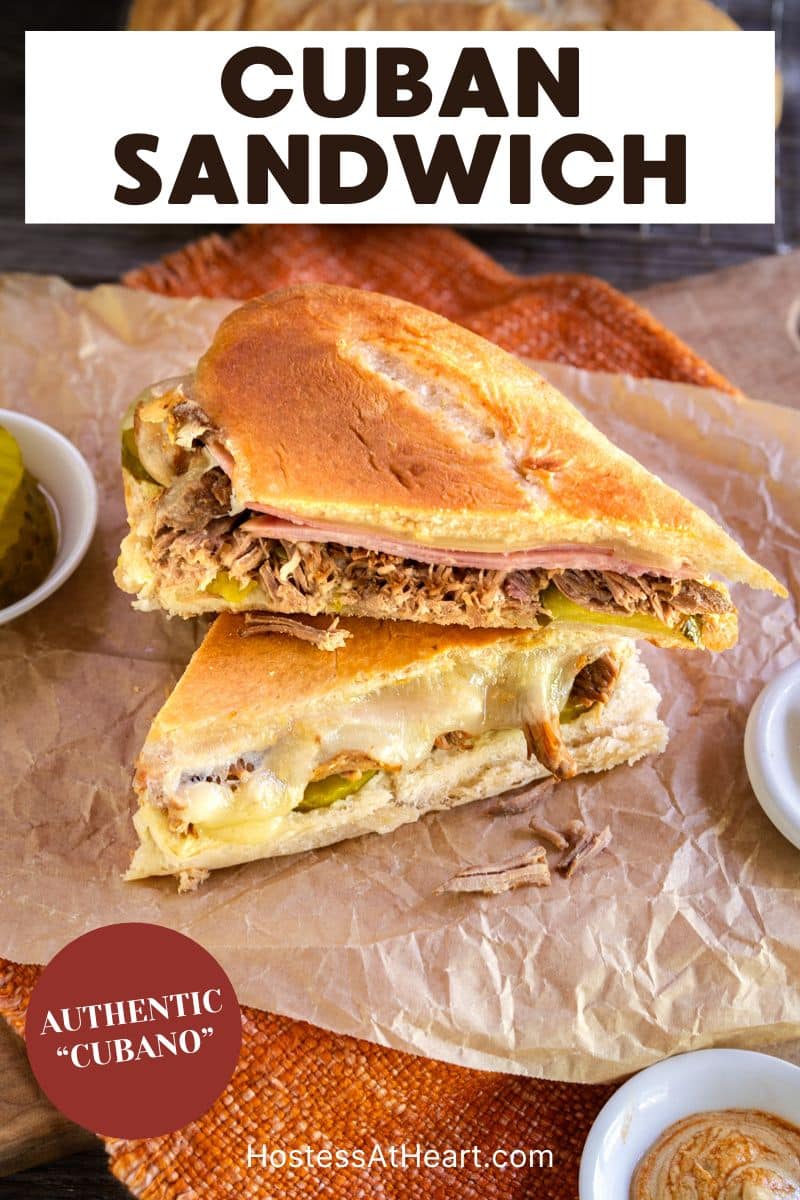 A authentic pressed Cuban Sandwich cut in half on parchment paper oozing with melted cheese over pork and ham. Hostess At Heart