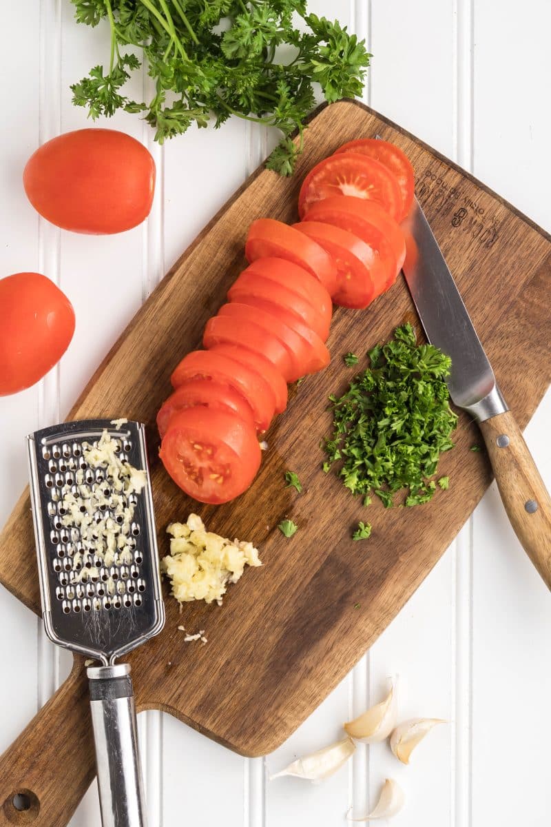 Sliced tomatoes, chopped parsley, and grated garlic on a cutting board. Hostess At Heart