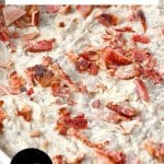 An image for Pinterest of creamy caramelized onion bacon dip topped with crispy bacon pieces in white serving bowl. Hostess At Heart